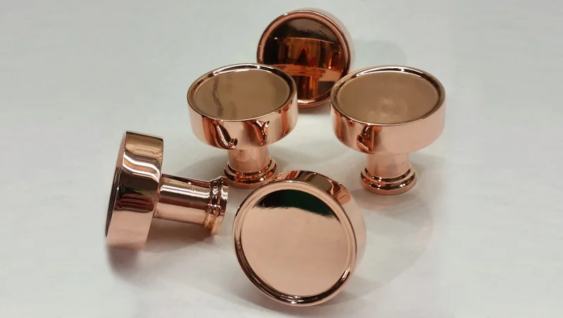 Five cupboard knobs in a polished copper finish, lying on a pale surface under raking light