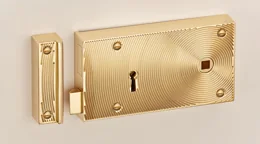 A polished brass rim lock with an engine turned face plate and a matching keep