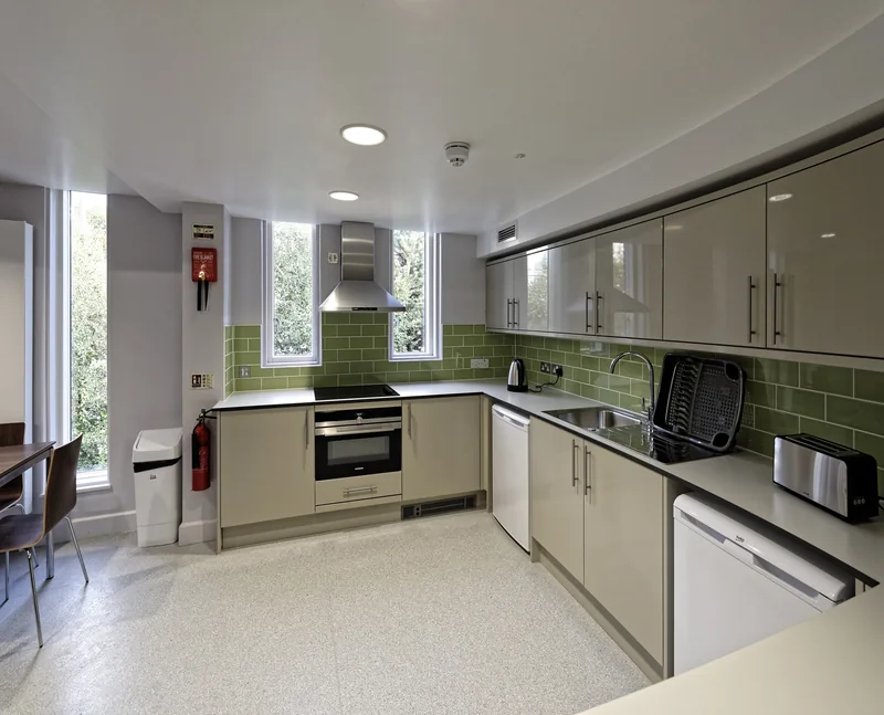 A fitted kitchen with wall units, a green tiled splashback and a door to the corridor