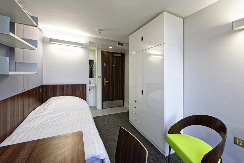 A study bedroom with a desk, chair and fitted storage beside a timber door