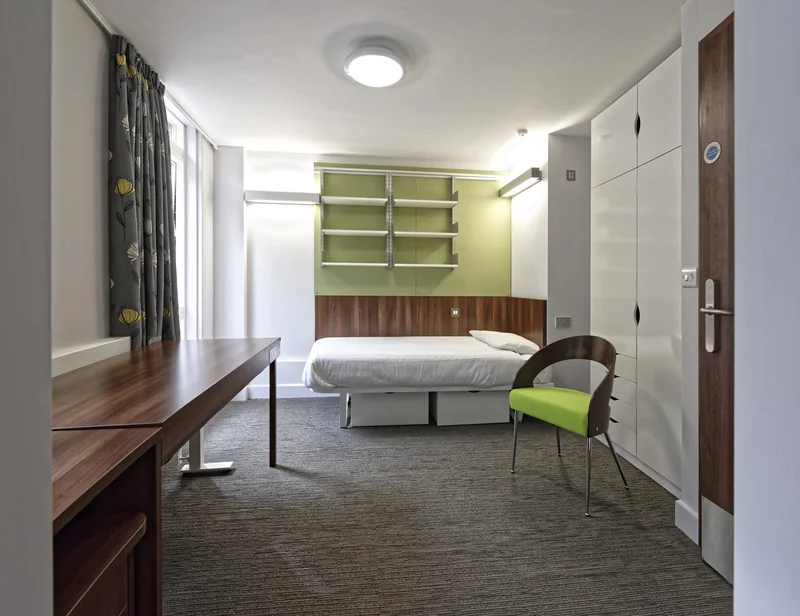 A study bedroom with a bed, desk and a timber door to the corridor
