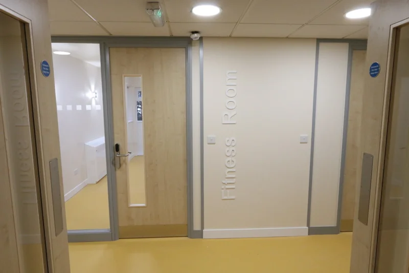 A corridor of timber doorsets with vision panels and lever furniture