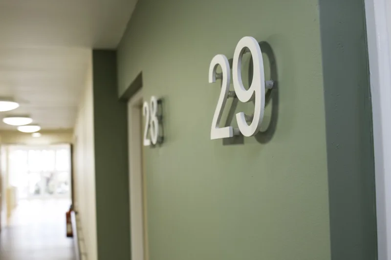 Large brushed metal numerals reading 28 and 29 fixed to a dark green corridor wall above door openings