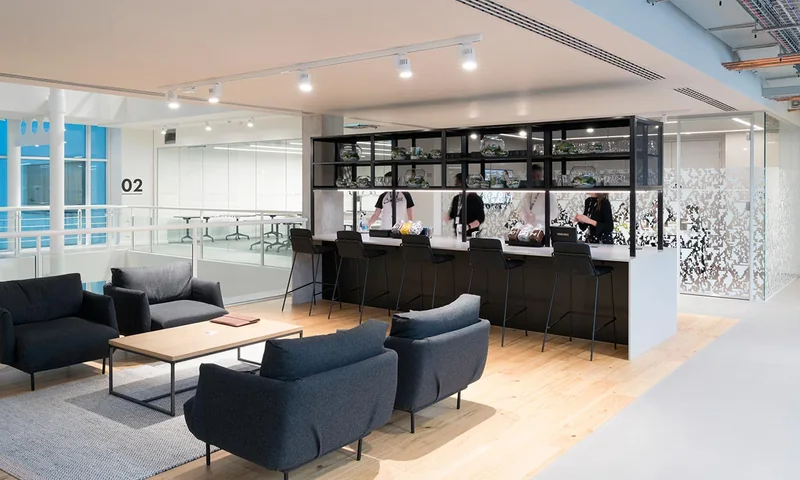 An office breakout floor with a coffee bar, high stools and a glazed meeting room beyond