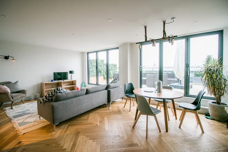 An apartment living room with a timber floor, dining table and glazed doors to a balcony