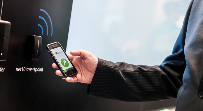 A hand holding a phone showing an unlock confirmation in front of a door mounted access control unit