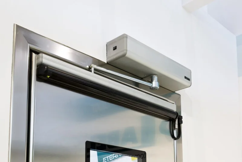 A surface mounted automatic door operator installed at the head of a glazed doorset, with the arm and track visible